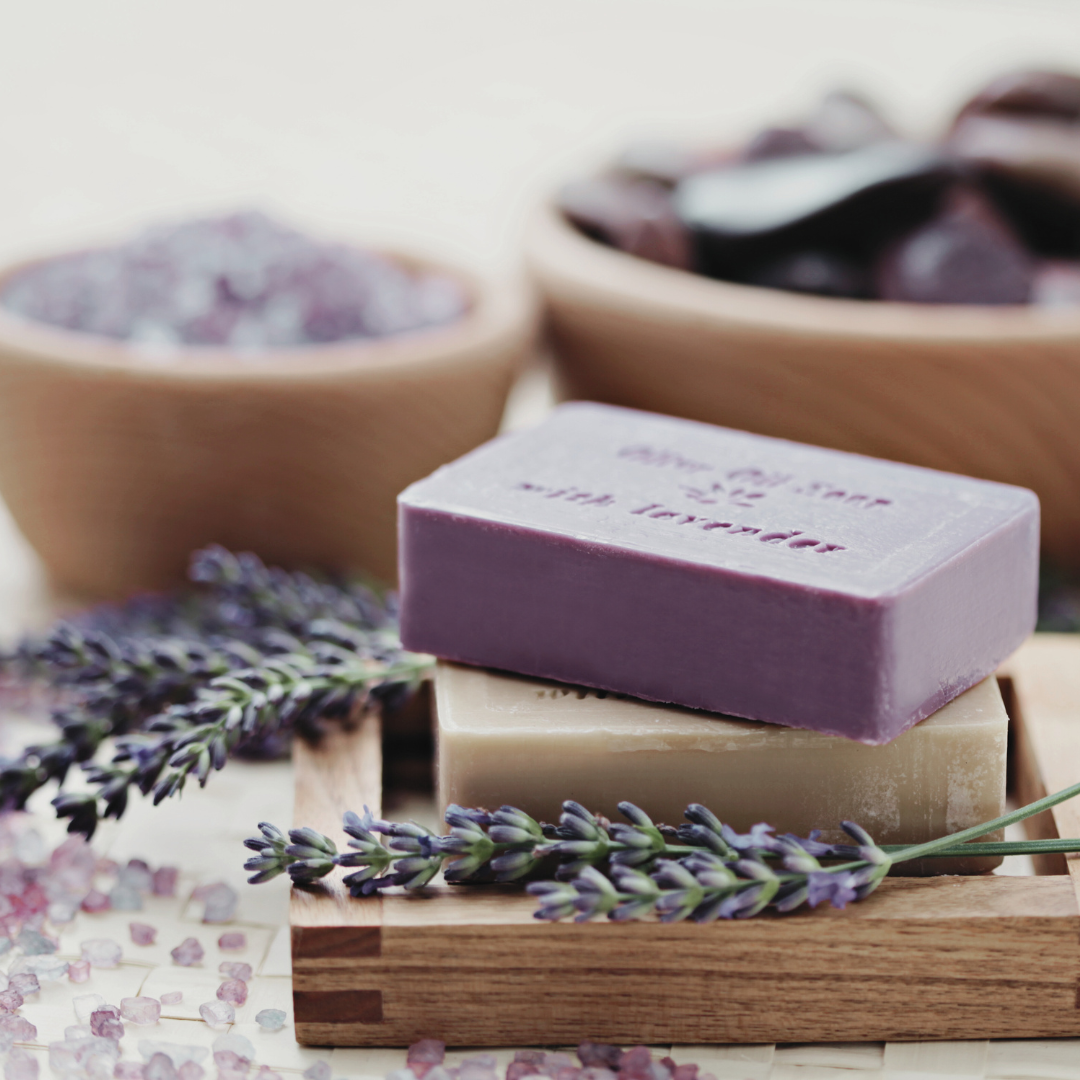 Two handmade soaps made with Lavender 'English', presented alongside harvested lavender flowers and foliage. The combination of natural ingredients and freshly picked lavender emphasizes the soothing and aromatic qualities of the soaps.